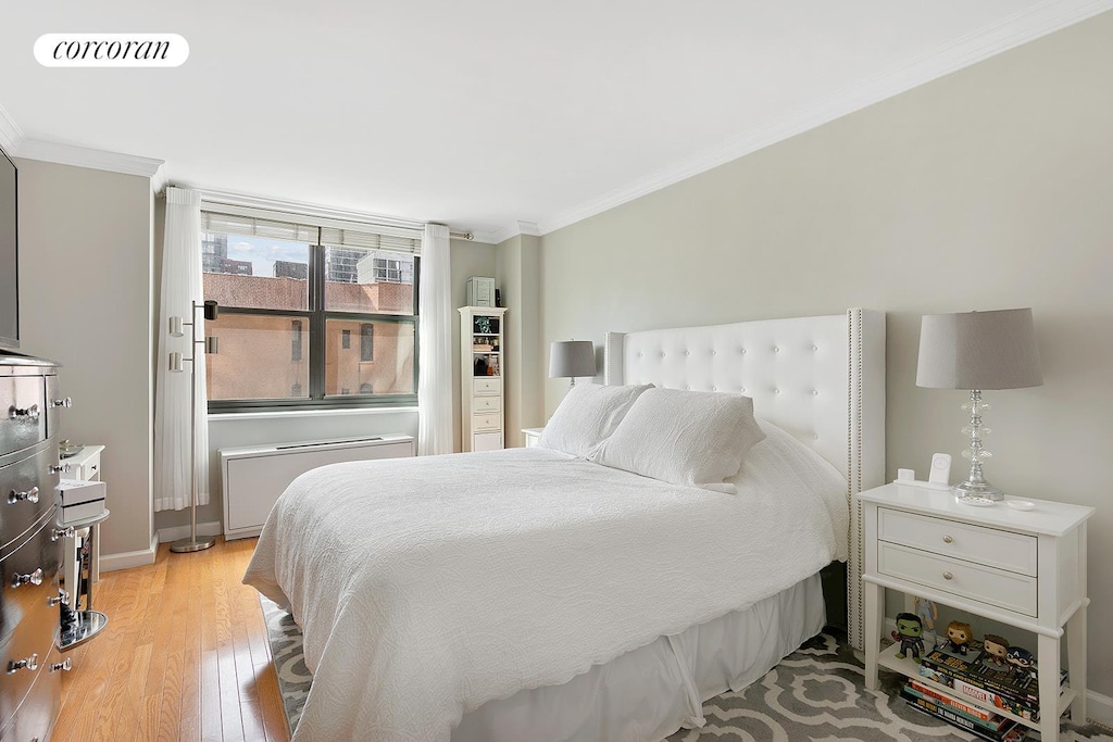 bedroom with ornamental molding, light wood-style flooring, radiator heating unit, and baseboards