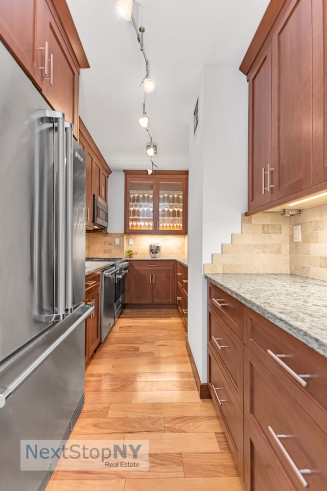 kitchen with appliances with stainless steel finishes, light wood-type flooring, light stone counters, tasteful backsplash, and brown cabinetry