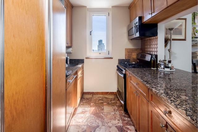 200 E 89th St Unit 27D, New York City, NY 10128 - kitchen featuring stainless steel appliances, brown cabinetry, dark stone counters, and baseboards