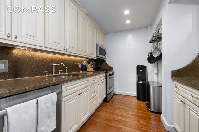 kitchen featuring appliances with stainless steel finishes, baseboards, tasteful backsplash, a sink, and wood finished floors
