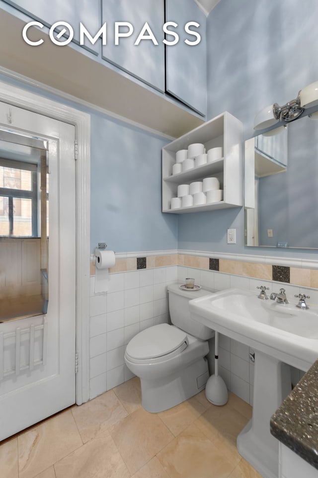 half bathroom with a wainscoted wall, toilet, and tile walls