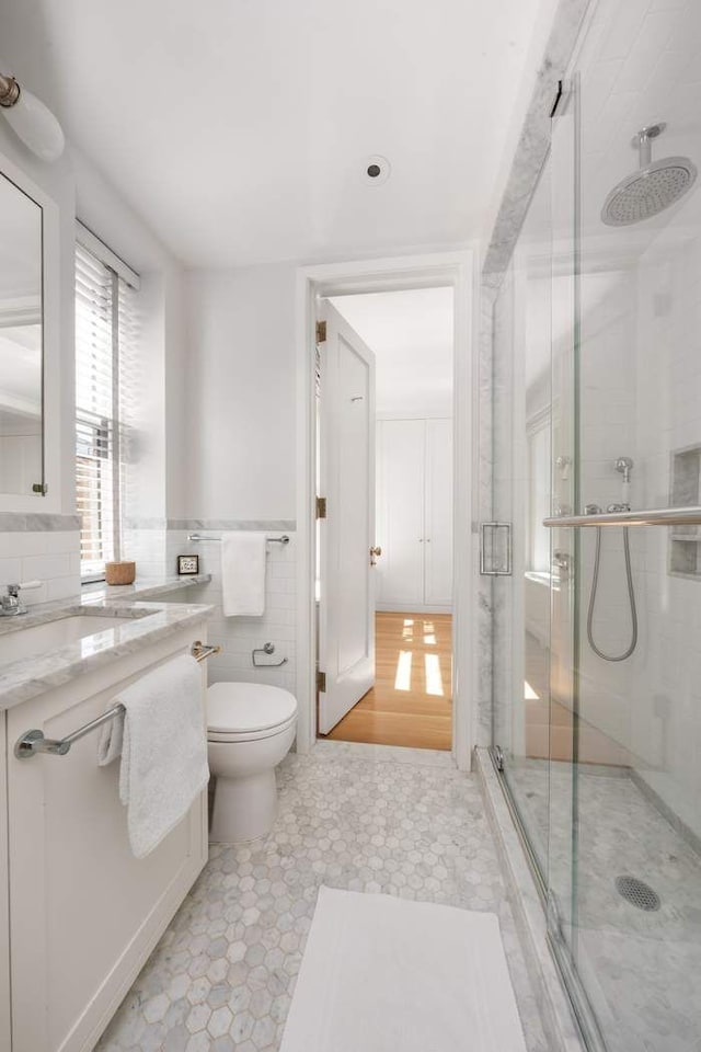 bathroom featuring a stall shower, toilet, tile patterned floors, a sink, and tile walls