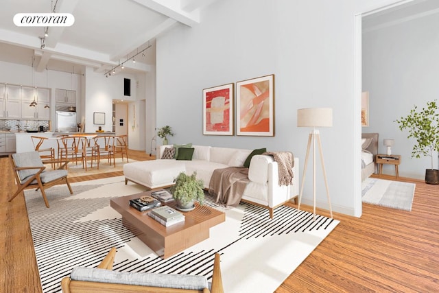 living area featuring rail lighting, a high ceiling, light wood-style floors, baseboards, and beamed ceiling