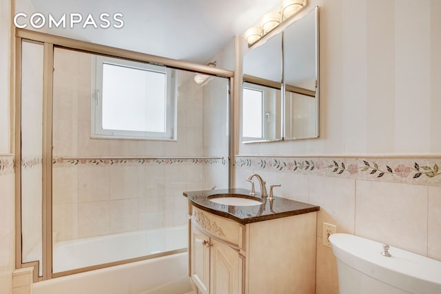 full bathroom with toilet, enclosed tub / shower combo, vanity, and tile walls
