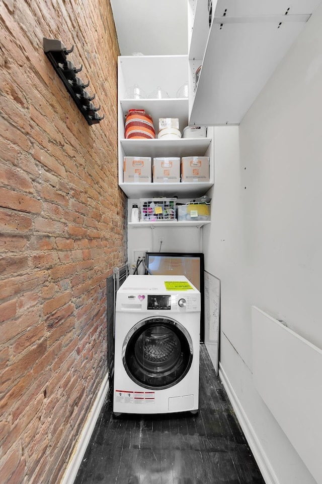 laundry room featuring washer / clothes dryer, brick wall, wood finished floors, and baseboards