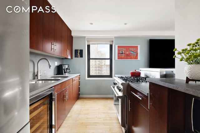 kitchen featuring appliances with stainless steel finishes, beverage cooler, light wood-style floors, a sink, and baseboards