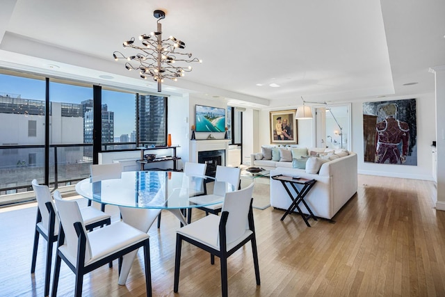 dining space with wood finished floors, a chandelier, baseboards, a glass covered fireplace, and recessed lighting