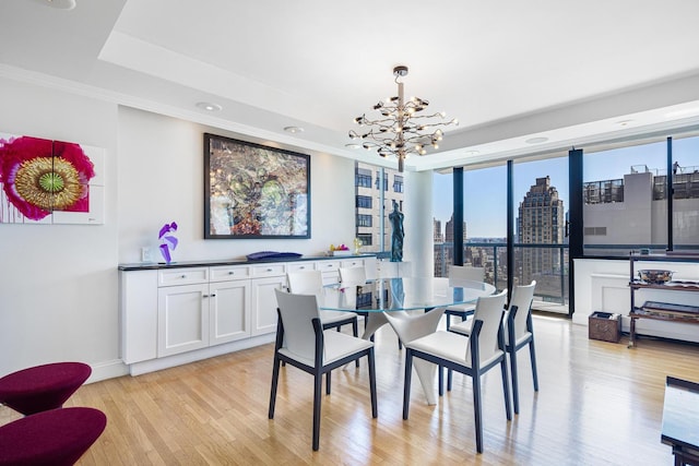 dining room featuring a chandelier, light wood-style flooring, a raised ceiling, crown molding, and a city view