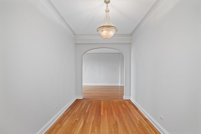 corridor with arched walkways, light wood-type flooring, and baseboards