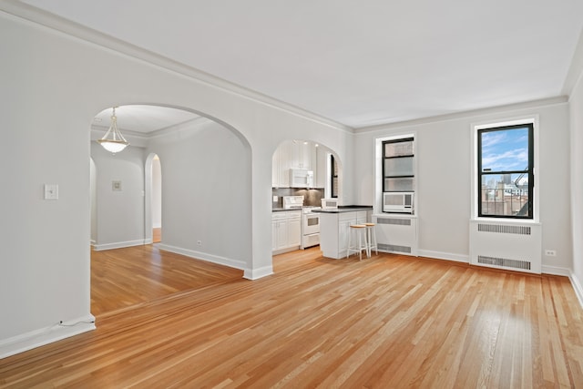 unfurnished living room featuring arched walkways, radiator, light wood finished floors, and crown molding