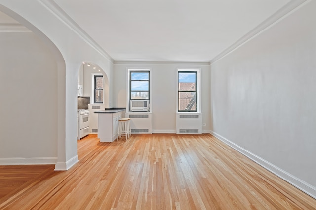 unfurnished living room featuring light wood-style flooring, radiator heating unit, arched walkways, crown molding, and cooling unit