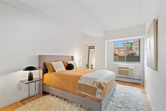 bedroom with a baseboard heating unit, wood finished floors, baseboards, and a textured ceiling