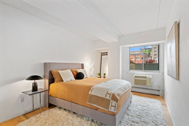 300 W 145th St Unit 1-N, New York City, NY 10039 - bedroom featuring baseboard heating, wood finished floors, baseboards, a wall mounted AC, and a textured ceiling