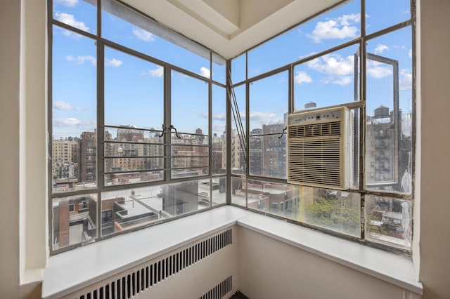 unfurnished sunroom with a city view, cooling unit, radiator heating unit, and healthy amount of natural light