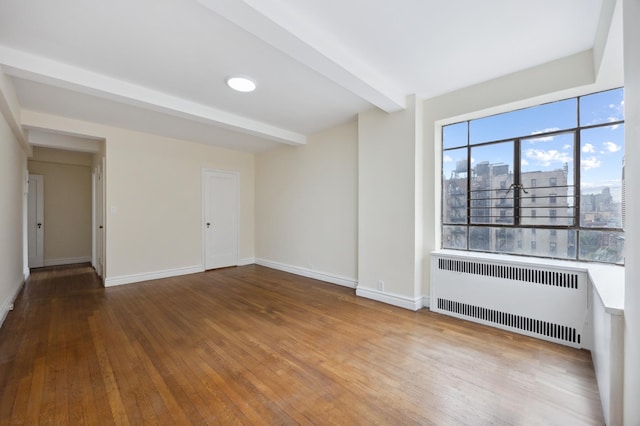 spare room featuring radiator, hardwood / wood-style flooring, baseboards, beamed ceiling, and a view of city