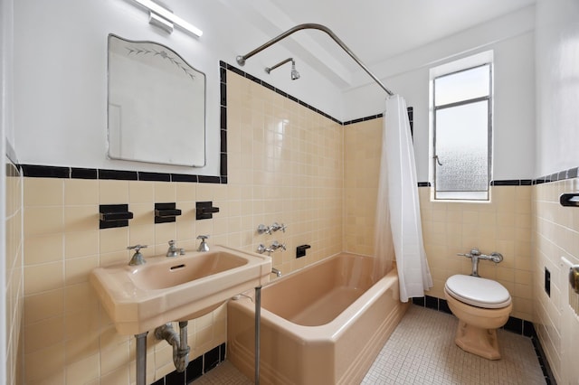 full bath featuring tile walls, tile patterned floors, toilet, shower / bath combo with shower curtain, and wainscoting