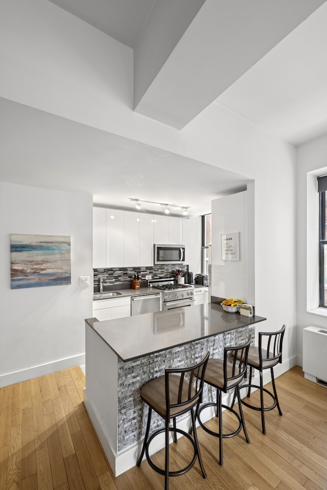 99 John St Unit 205, New York City, NY 10038 - kitchen with appliances with stainless steel finishes, modern cabinets, a sink, a kitchen bar, and white cabinetry