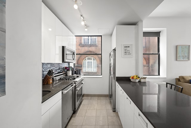 99 John St Unit 205, New York City, NY 10038 - kitchen featuring appliances with stainless steel finishes, dark countertops, white cabinets, tasteful backsplash, and light tile patterned flooring