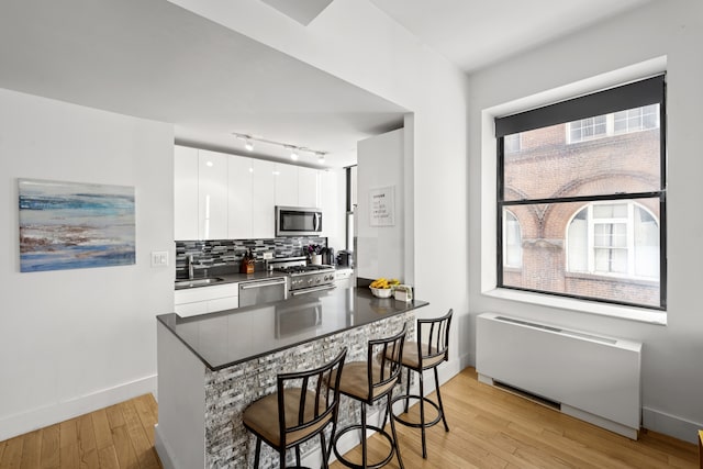 99 John St Unit 205, New York City, NY 10038 - kitchen featuring stainless steel appliances, a kitchen bar, white cabinets, dark countertops, and light wood-style flooring