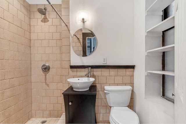 bathroom featuring a tile shower, toilet, vanity, and tile walls