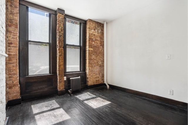 spare room featuring radiator heating unit, dark wood-style flooring, and baseboards