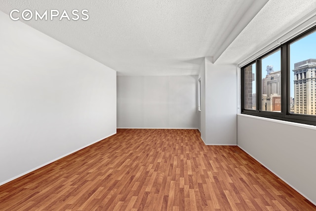 spare room with wood finished floors, a textured ceiling, and baseboards