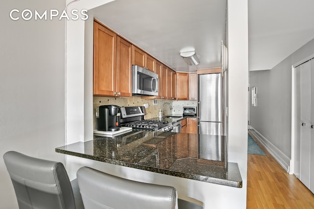 350 E 62nd St Unit 4B, New York City, NY 10065 - kitchen with stainless steel appliances, a sink, a peninsula, light wood-type flooring, and dark stone counters