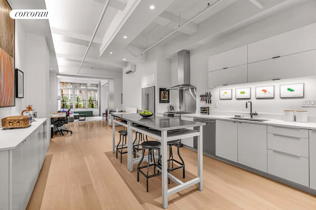 kitchen with modern cabinets, wall chimney exhaust hood, appliances with stainless steel finishes, a sink, and an AC wall unit