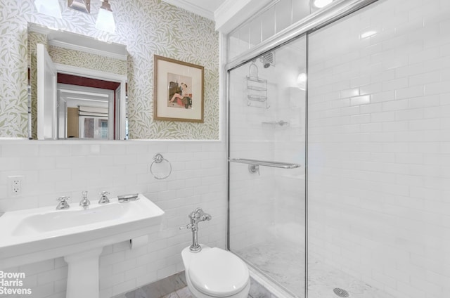 full bath featuring wallpapered walls, a stall shower, wainscoting, crown molding, and a sink