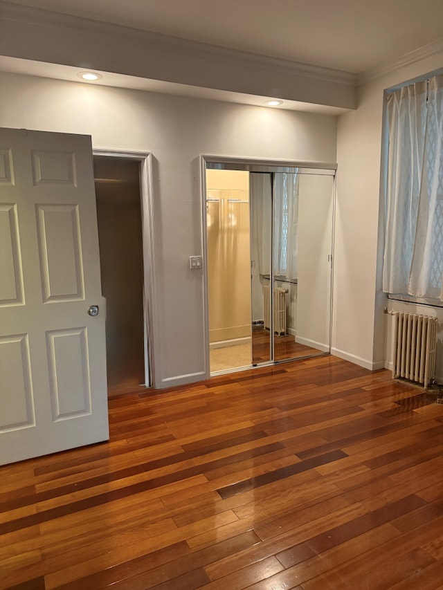 57 W 58th St Unit 3H, New York City, NY 10019 - unfurnished bedroom featuring radiator heating unit, crown molding, wood-type flooring, a closet, and baseboards