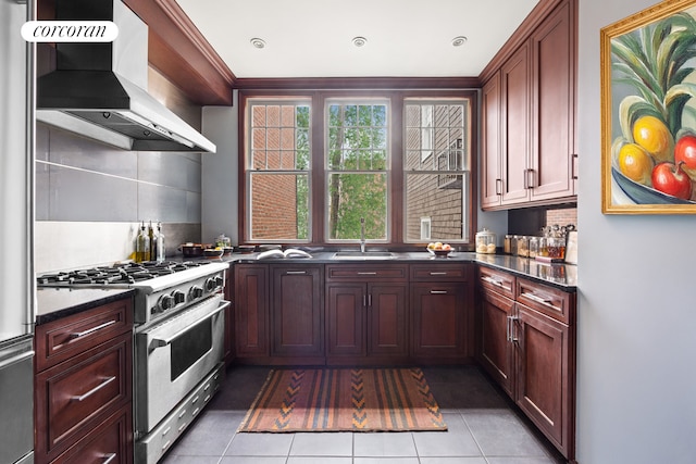 kitchen featuring appliances with stainless steel finishes, wall chimney range hood, a sink, light tile patterned flooring, and tasteful backsplash