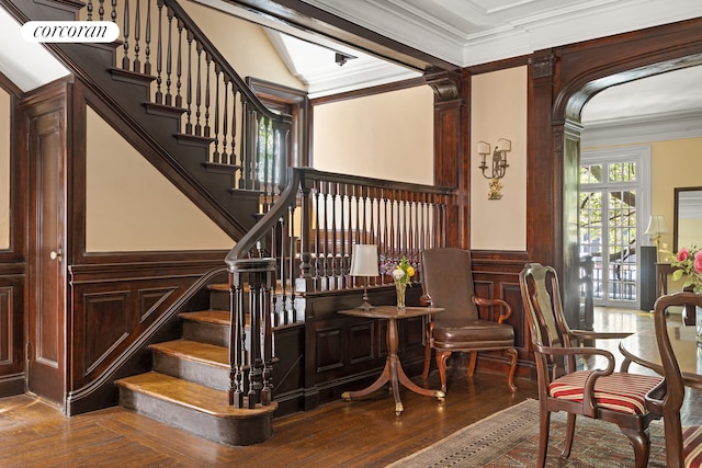 stairway with wood finished floors, a decorative wall, crown molding, and wainscoting