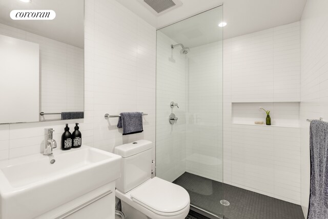 bathroom with tile walls, toilet, tiled shower, vanity, and recessed lighting