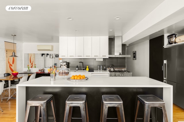 kitchen with high end refrigerator, a sink, wall chimney range hood, a wall mounted AC, and a kitchen breakfast bar