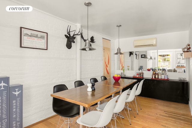 dining room with a wall unit AC, light wood-style flooring, and brick wall