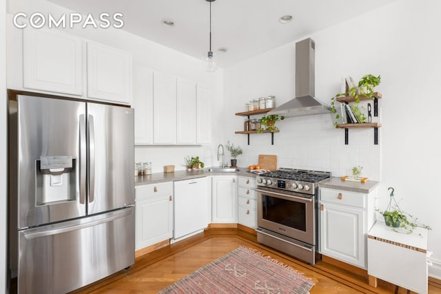 kitchen featuring stainless steel appliances, open shelves, wall chimney exhaust hood, a sink, and white cabinetry