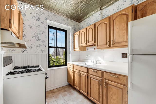 kitchen with white appliances, wallpapered walls, a sink, light countertops, and under cabinet range hood