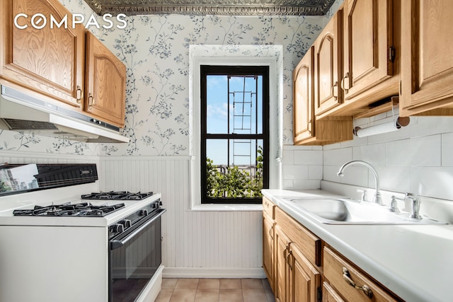 kitchen with white range with gas cooktop, wallpapered walls, under cabinet range hood, a sink, and light countertops