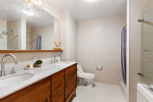 bathroom with tile walls, tile patterned floors, tiled shower, toilet, and double vanity
