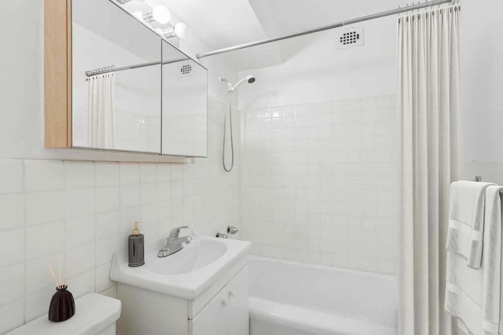 bathroom featuring shower / tub combo with curtain, tasteful backsplash, toilet, vanity, and tile walls