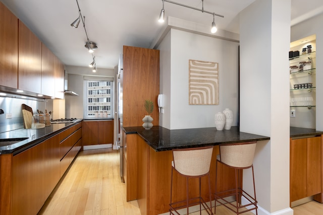 411 E 53rd St Unit 19D, New York City, NY 10022 - kitchen featuring track lighting, a peninsula, light wood-type flooring, brown cabinetry, and a breakfast bar area