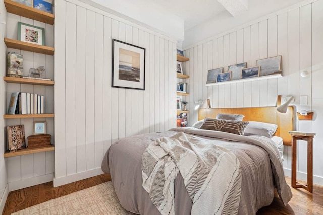 bedroom featuring wood finished floors, wood walls, baseboards, and beamed ceiling