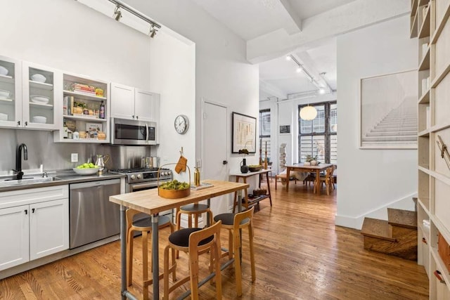 kitchen featuring track lighting, appliances with stainless steel finishes, a sink, open shelves, and beam ceiling