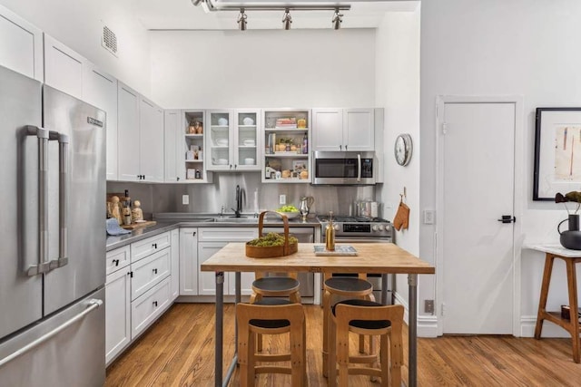 kitchen with stainless steel appliances, rail lighting, open shelves, wood finished floors, and a high ceiling