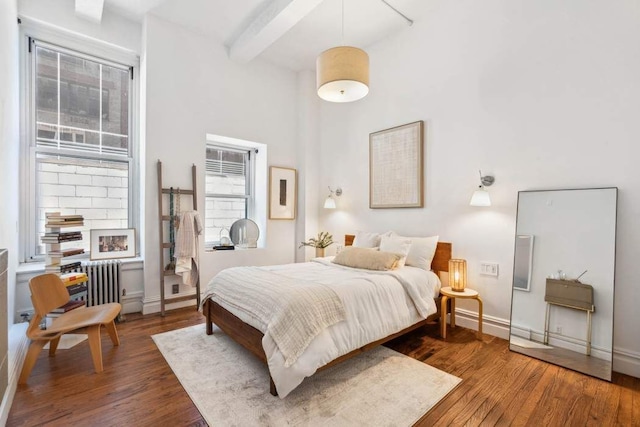 bedroom featuring wood finished floors, beamed ceiling, a towering ceiling, baseboards, and radiator heating unit