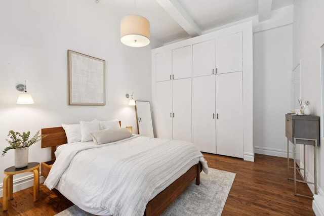 bedroom with beamed ceiling, dark wood-style floors, a closet, and baseboards