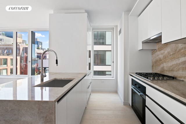 450 Washington St Unit 705, New York City, NY 10013 - kitchen featuring oven, stainless steel gas cooktop, light wood-style flooring, exhaust hood, and decorative backsplash