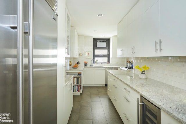 kitchen featuring high end fridge, beverage cooler, backsplash, a sink, and white cabinets