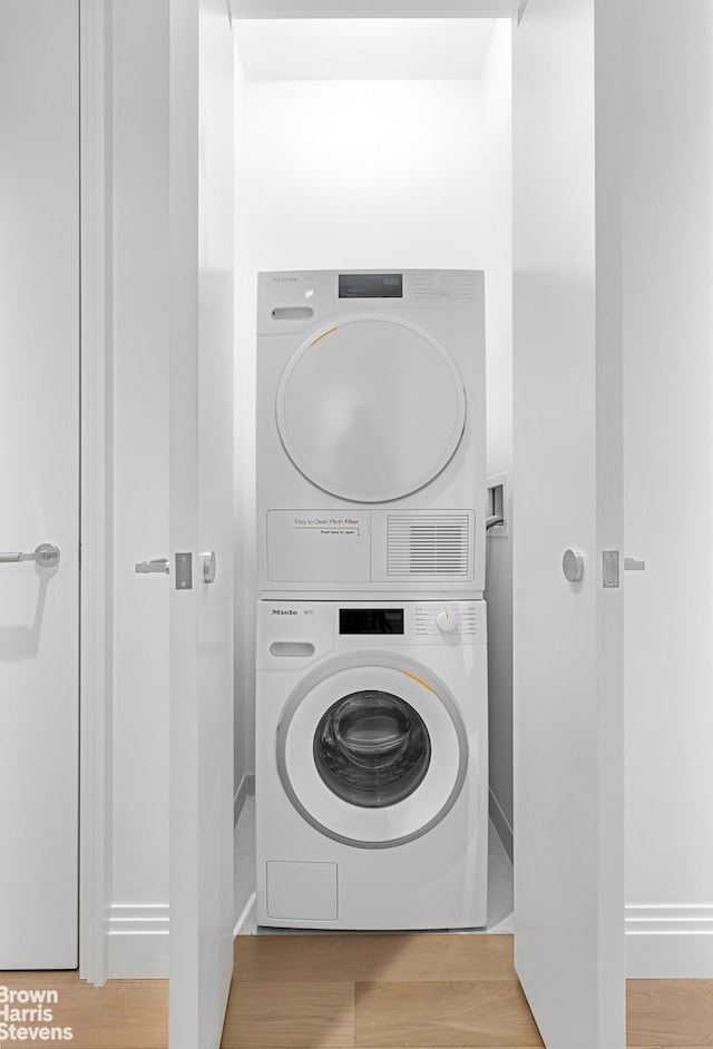 washroom with stacked washing machine and dryer and wood finished floors