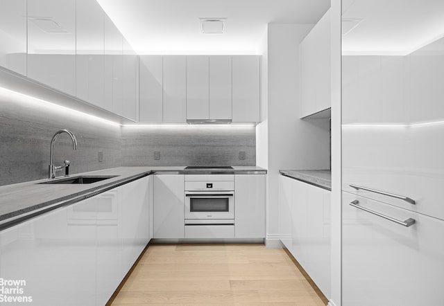kitchen with modern cabinets, white oven, a sink, white cabinetry, and decorative backsplash